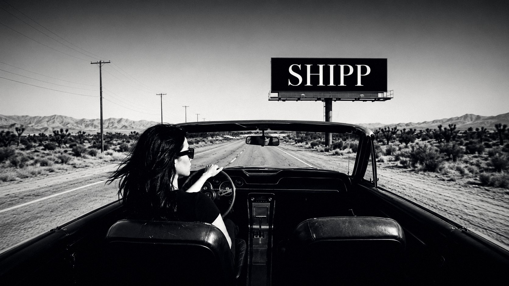 A woman driving a convertible down an open desert highway toward a Shipp Outdoor billboard